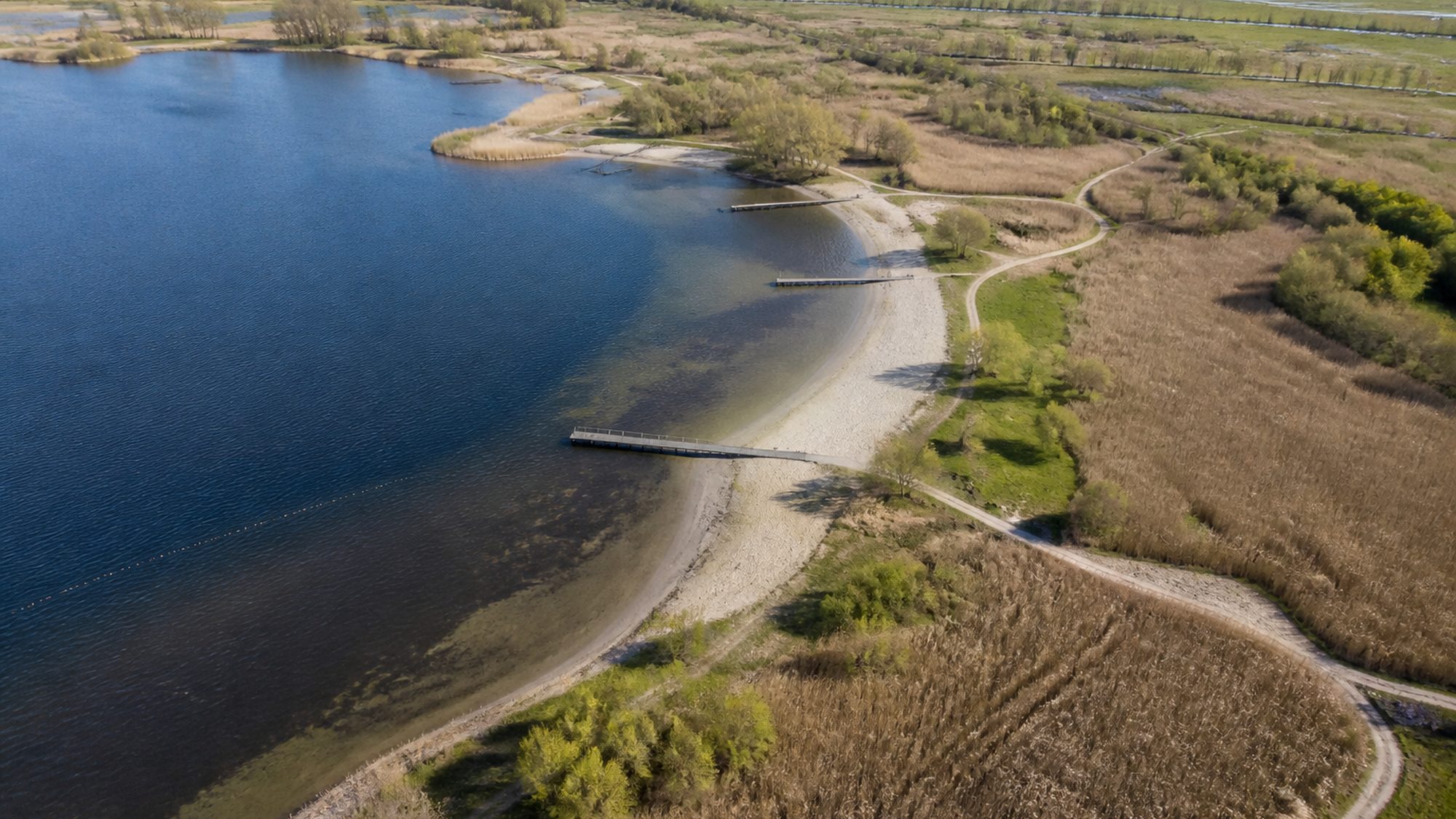 Recreatieplas met zandstranden, houten steigers en paden door het riet