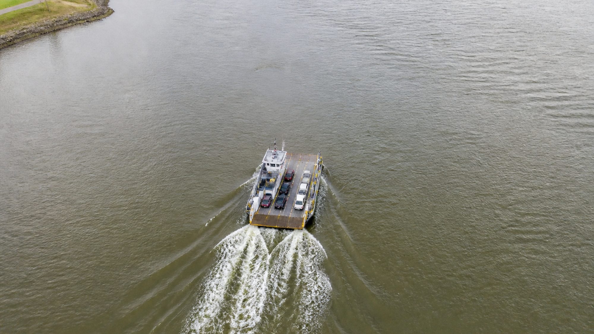 Kleine veerpont die een brede rivier oversteekt met een spreidend kielzog