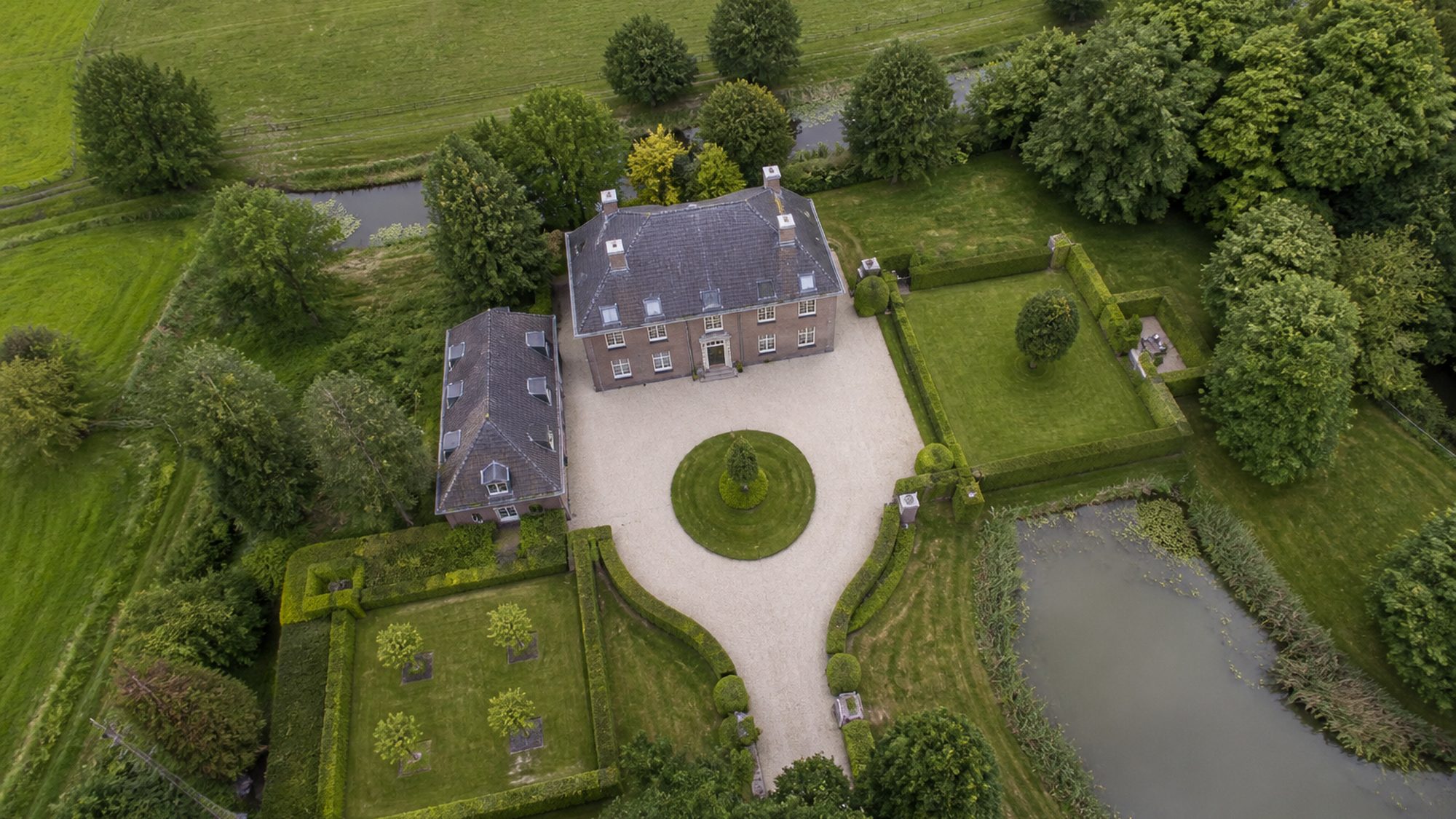 Landhuis met grindoprit, geschoren hagen en een vijver, schuin van boven