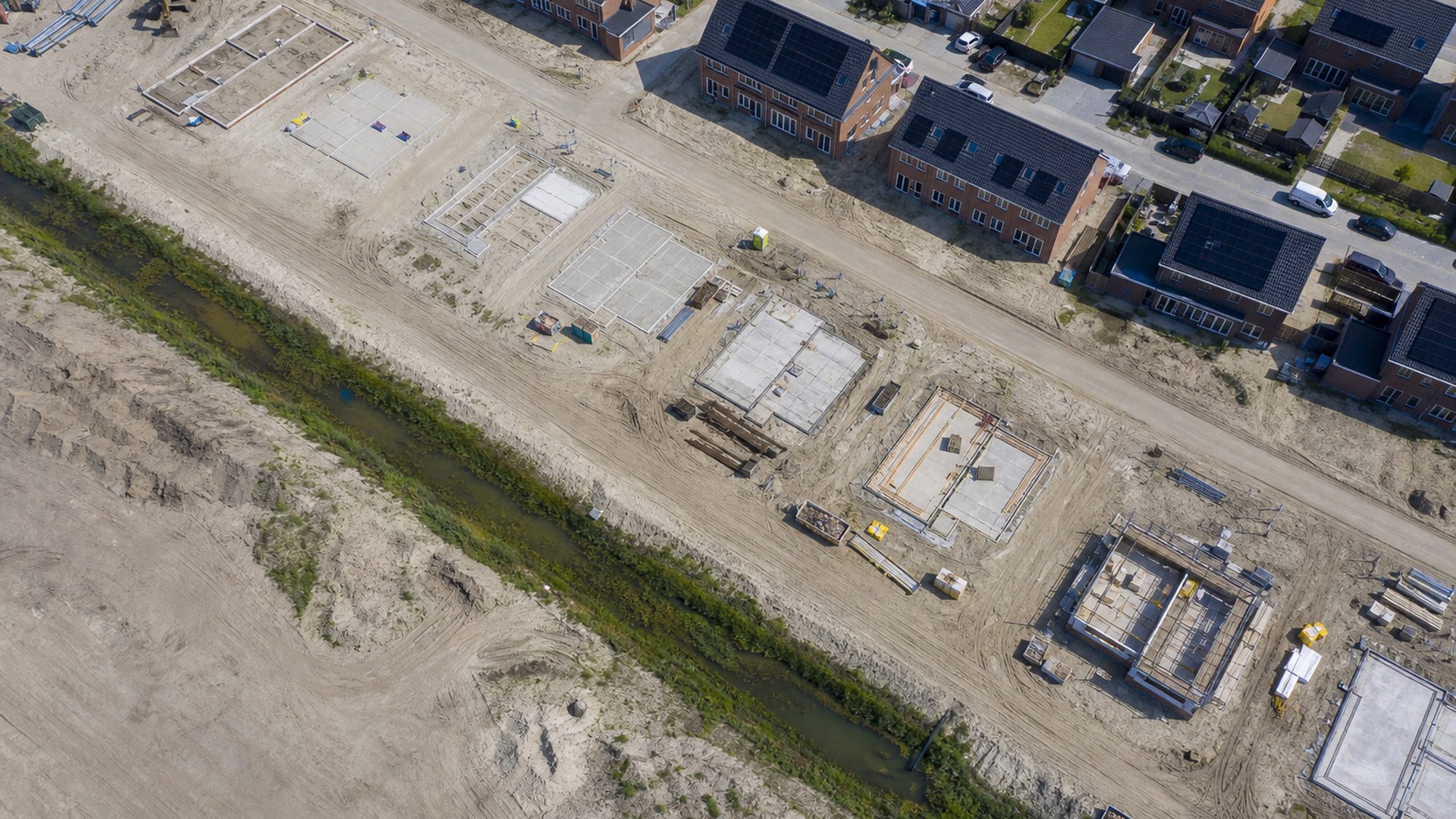 Nieuwbouwwijk in aanbouw met kale zandkavels en pas gelegde daken