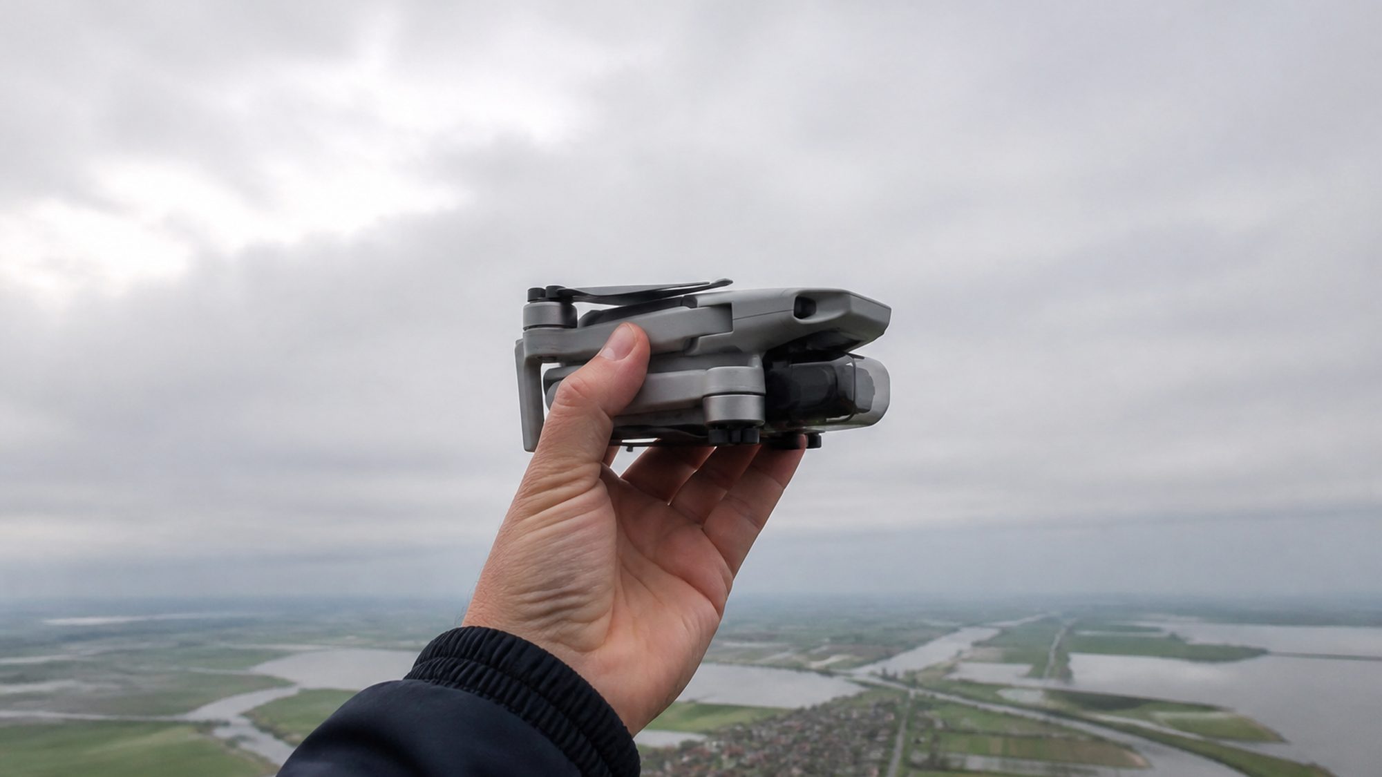 Een hand houdt een kleine opgevouwen drone omhoog tegen een bewolkte lucht