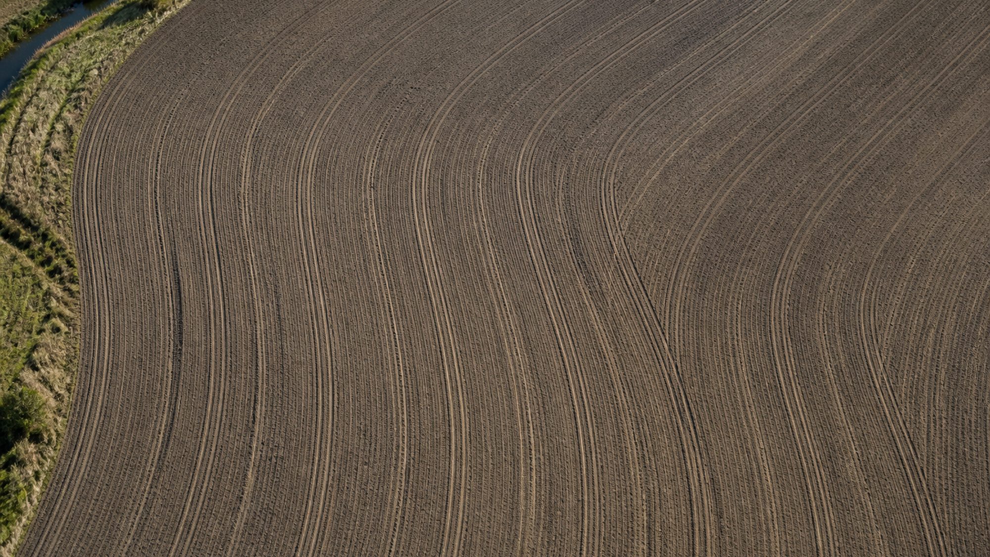Geploegde akker recht van boven met evenwijdige tractorsporen