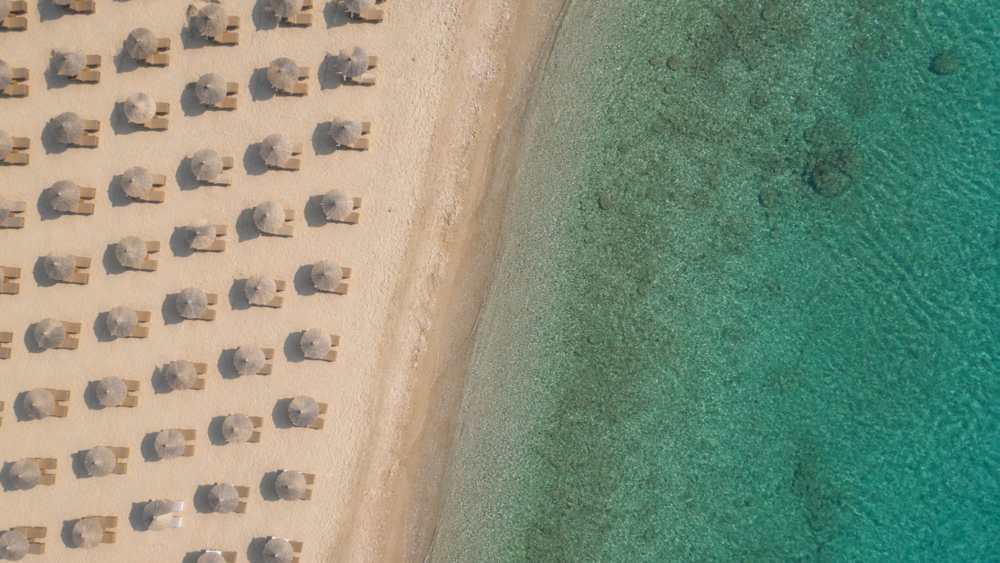 Grieks strand recht van boven met rijen ligbedden en rieten parasols